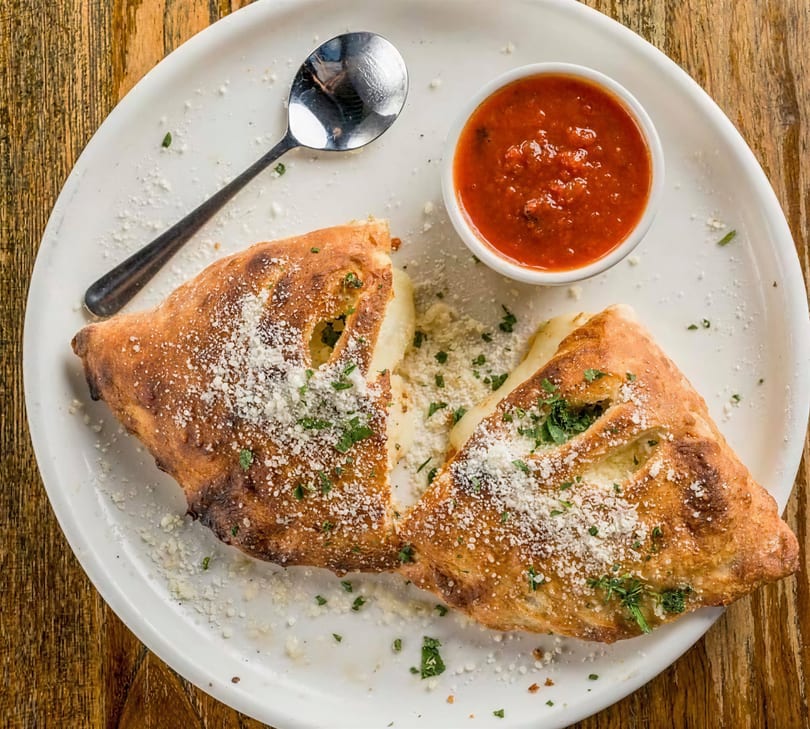 Golden-brown calzone halves with melted cheese, parmesan, and parsley, served with a side of marinara.