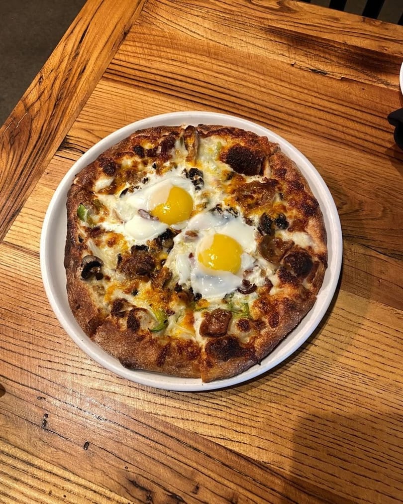 Breakfast pizza with two fried eggs, melted cheese, mushrooms, and green peppers on a white plate.