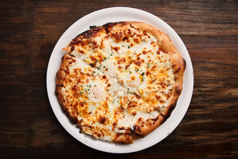 Sliced pizza with melted cheese, baked eggs, and green herbs on a white plate.