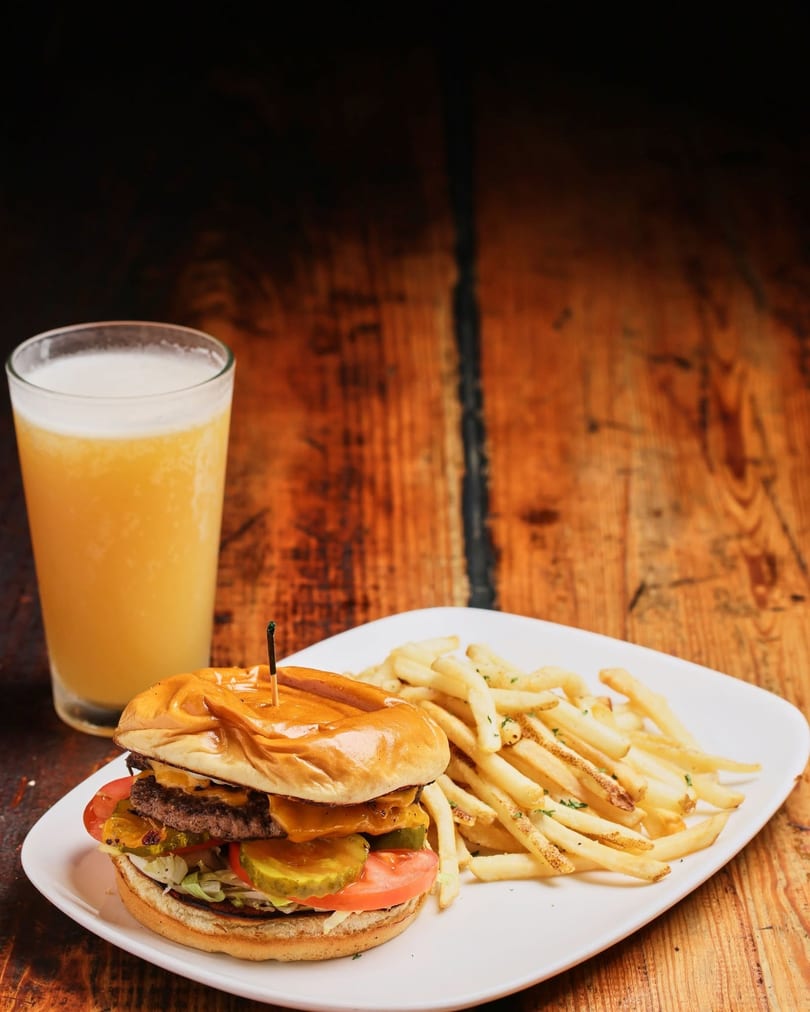 Juicy double cheeseburger with fries and a refreshing beer on a rustic wooden table.